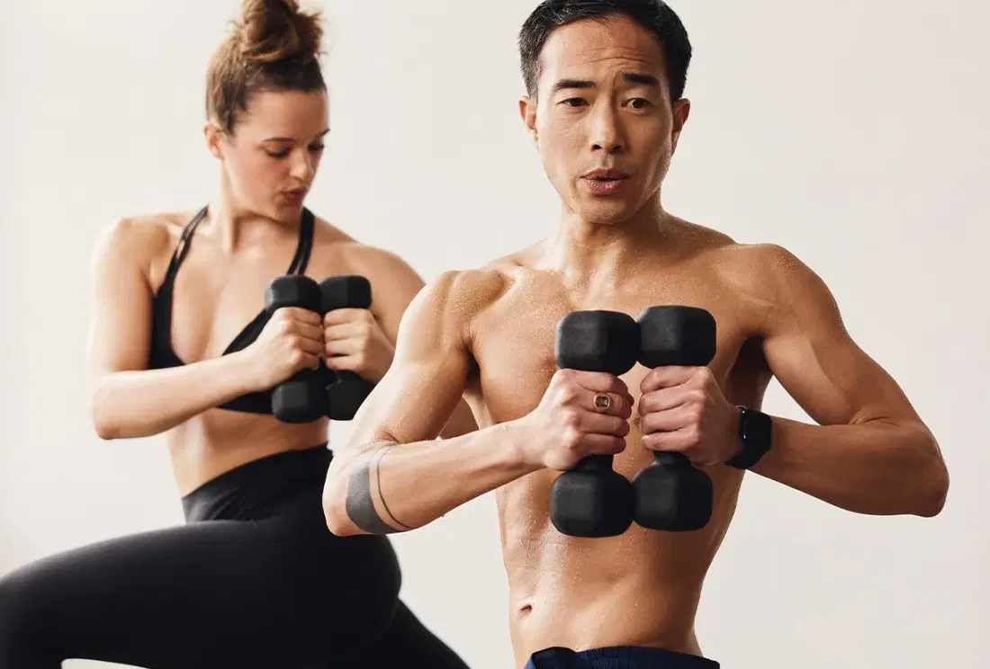 Two yogis in a twisted lunge position each holding black dumbbells close to their chests