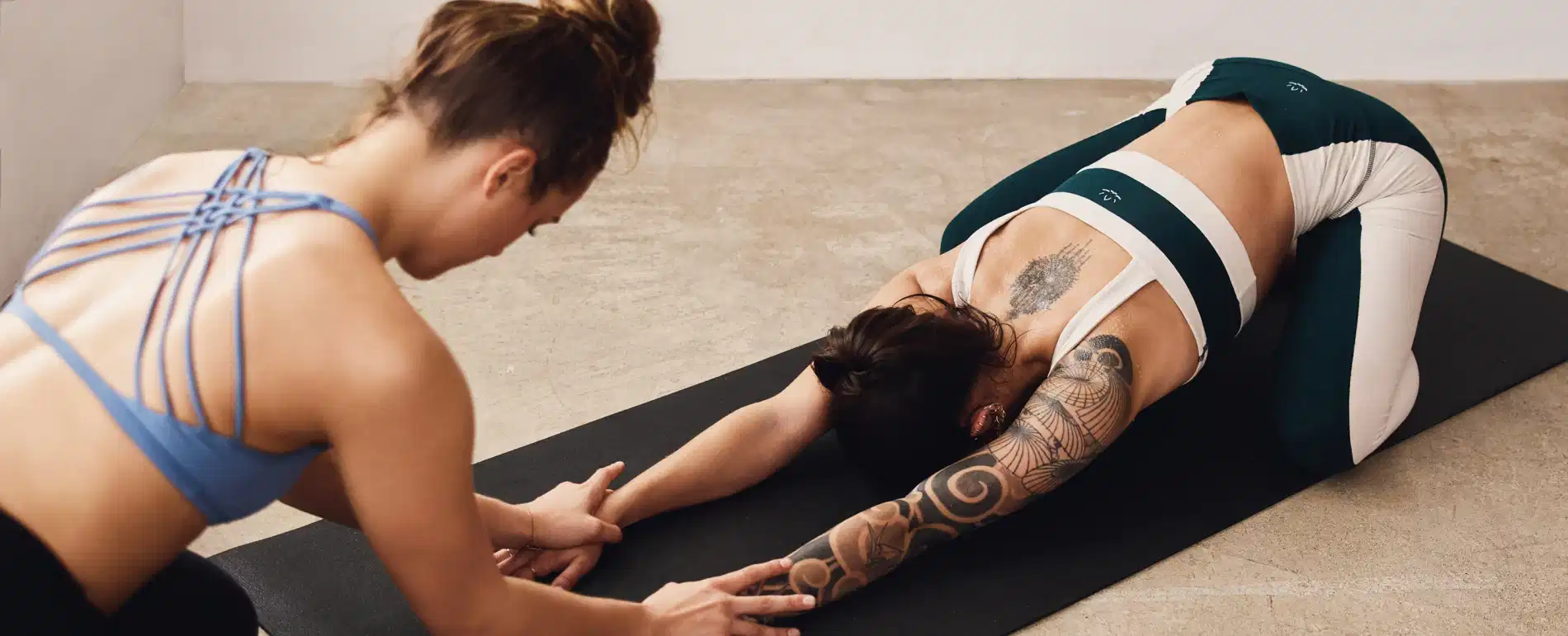 Yoga teacher providing corrections to a student in a child's pose