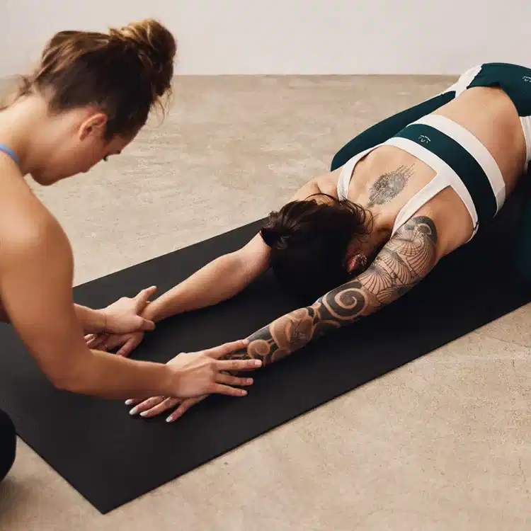 Yoga teacher providing corrections to a student in a child's pose