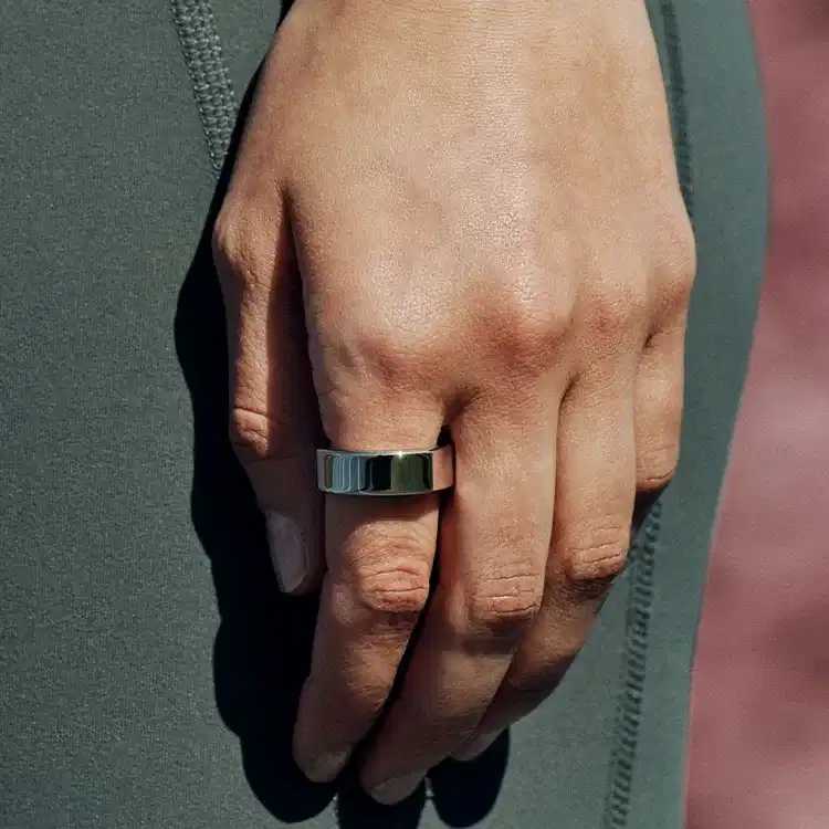 Woman wearing forest green leggings with her hands and arms by her side with a silver Oura Ring on her index finger